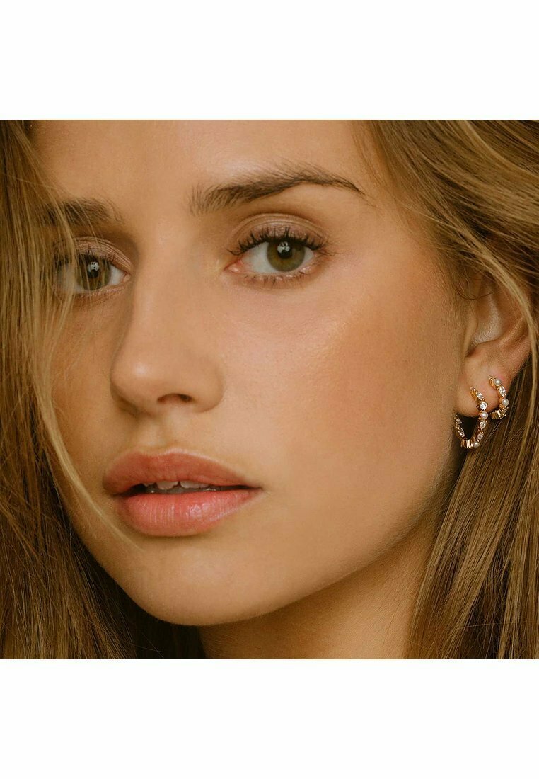 Orecchini ad anello color oro decorati con pietre trasparenti e brillanti; finitura liscia; vista ravvicinata di un modello che li indossa con capelli lunghi e mossi.