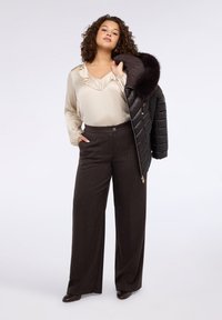 Jasnobeżowa satynowa bluzka z falbankowym dekoltem, zestawiona z ciemnobrązowymi, szerokimi spodniami z złotymi drobinkami. Na ramieniu zarzucona czarna puchowa kurtka.