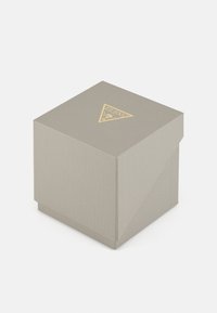 Grå texturerad presentlåda med en gyllene triangel-logotyp. Lådan har ett lock som viks ner, vilket skapar en minimalistisk design.