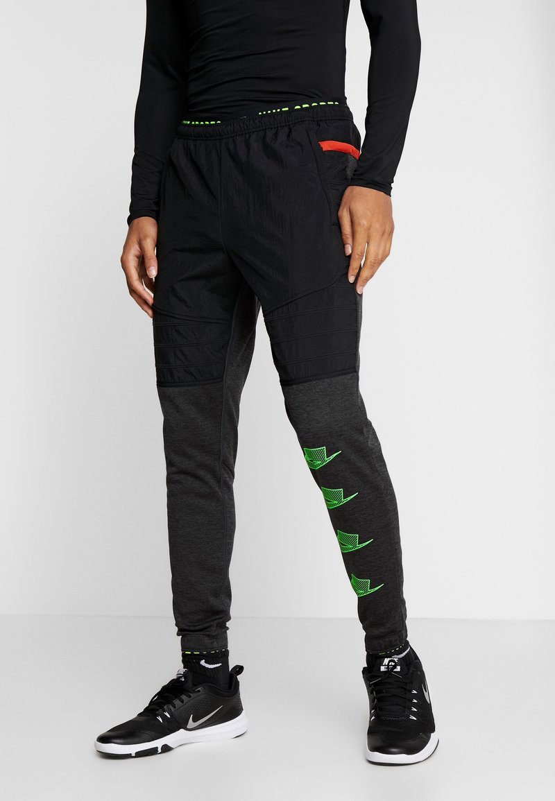 Schwarze und graue Jogginghosen mit strukturierten Einsätzen, einem grünen Logodetail am Bein und einem elastischen Bund mit roten Akzenten.