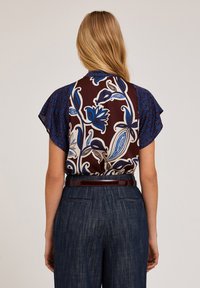 Brun och blå mönstrad blus med vågiga ärmar, med blommiga och paisleymönster, bärs med högmidjade marinblå byxor och ett mörkt bälte.