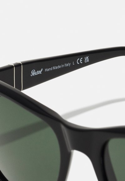 Óculos de sol Persol pretos com lentes verdes, apresentando um design elegante, detalhes em dourado nas hastes e a inscrição "Feito à Mão na Itália".