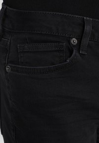 Jeans de mezclilla negra con un bolsillo frontal, diseño clásico de cinco bolsillos, costuras resistentes y cierre de botón metálico en la cintura.