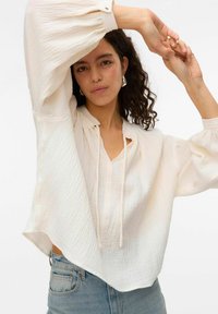 Vit, texturerad blus med V-ringning, dragsnodd och puffärmar, i kombination med hög midja blå jeans. Mjukt, lätt material.