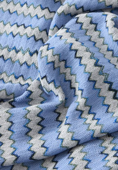 Tissu tricoté doux avec un motif en zigzag bleu clair, blanc et bleu foncé, montrant des plis et des détails de texture.