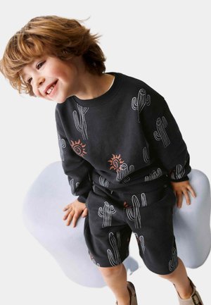 Zwart sweatshirt en shortset met cactussen en zonpatronen in wit en oranje. De stof lijkt zacht en heeft een losse pasvorm.