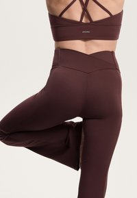Burgundi sportleggings és egy hozzáillő sportmelltartó, sima, rugalmas anyagból, keresztpántos hátrésszel és magas derékkal.