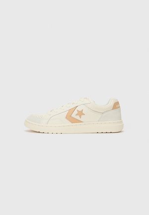Sneaker bianca low-top con stella beige e logo a chevron sul lato, lacci bianchi e dettaglio beige sul tallone su sfondo chiaro.