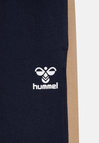 Marinblått och beige tyg med vitt Hummel-logo, som visar en stiliserad bi och varumärkesnamnet på den marinblå sektionen.