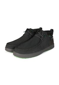 Zapatos de ante negro con un diseño curvado, costuras blancas que contrastan y un forro suave. La suela es de goma oscura con detalles en verde.