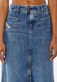 Denim rok in lichtblauw met twee voorzakken, knoopsluiting en voorsplit. Heeft gestikte details en een licht vervaagde structuur.