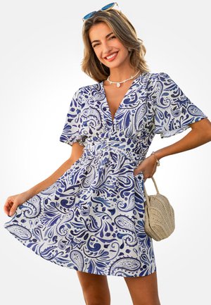 Biała sukienka z niebieskim wzorem paisley, krótkimi rękawami i talią podkreśloną paskiem. Posiada rozkloszowaną spódnicę oraz okrągłą plecioną torebkę jako dodatek.