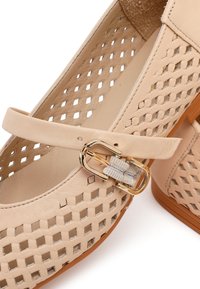 Beige dames platte schoen met geweven lederen ontwerp, gesloten neus, enkelriem en gouden gesp.