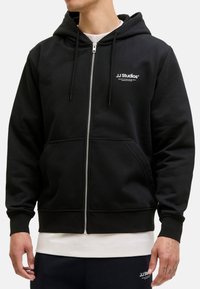 Felpa nera con zip realizzata in tessuto misto cotone, con logo frontale, cappuccio con cordino e tasche frontali. Finitura texturizzata con polsini a coste.