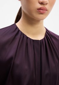 Lila Bluse mit rundem Ausschnitt und plissierten Details, glatter Textur und leicht lockerer Passform an den Schultern.