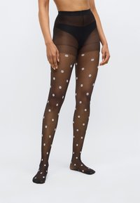 Μαύρες διάφανες κάλτσες με κεντήματα λουλουδιών, με ψηλή μέση και κάλυψη αστραγάλου, διακοσμημένες με λευκά λουλούδια σε όλη την επιφάνεια.