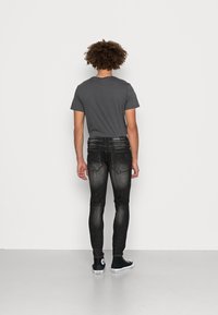 Szara koszulka, obcisłe czarne jeansy i czarne trampki Converse. Jeansy mają wyblakły wygląd i delikatne przeszycie na tylnej kieszeni.