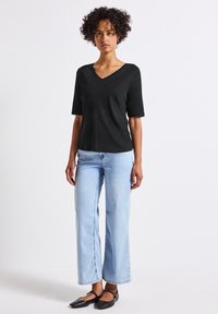 Černý top s krátkým rukávem a výstřihem do V, v kombinaci se světlými modrými kalhotami s širokými nohavicemi a černými balerínami. Hladká textura látky, neformální design.