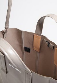 Borsa a tote in pelle beige con una texture liscia, dotata di un ampio interno foderato e dettagli in pelle marrone a contrasto. Include un particolare logo.
