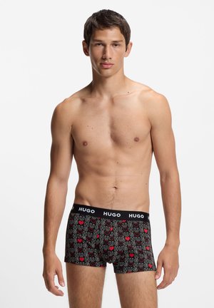 Black boxer shorts featuring a playful multi-colored "HUGO" and heart pattern on stretch fabric, with a black elastic waistband.