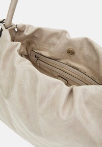 Borsa a spalla beige trapuntata con una texture morbida, dotata di una tasca interna con zip e chiusura a scatto. Foderata con un motivo "Guess".