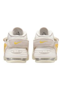 Adidași albi și beji cu guler căptușit, accente galbene, curele reglabile și o amortizare a aerului vizibilă în talpa transparentă.
