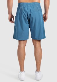 Shorts deportivos azules con una cintura elástica, con un panel trasero texturizado. Combinados con zapatillas blancas.