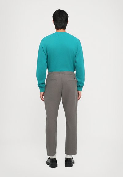 Teal sweatshirt made of cotton, paired with grey trousers featuring back pockets. The pants have a tailored fit ending above the ankles.