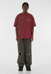 Maroon oversized t-shirt with short sleeves and front logo, paired with loose-fitting distressed black jeans featuring large holes.