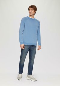 Heller blauer Rundhalspullover aus Strickstoff, kombiniert mit blauen Jeans und grauen Sportschuhen. Die Passform ist lässig mit einer entspannten Silhouette.