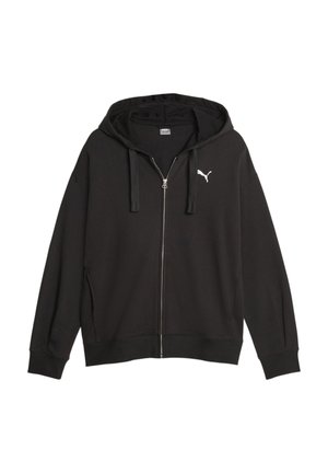 Czarny brzeg bluzy Puma z metką marki noszony na jasnoniebieskich dżinsach na szarym tle.