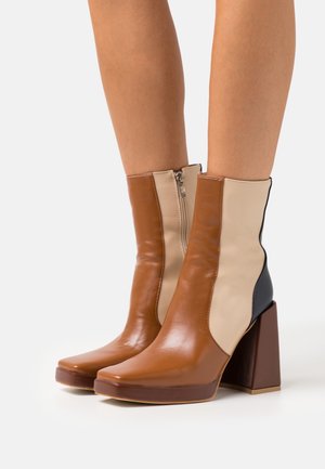 Bottes chevilles marron et beige avec bout carré, talon carré haut, et fermeture éclair latérale ; cuir lisse avec design bicolore.