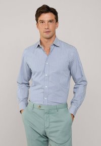 Blauw-wit gestreepte overhemd met lange mouwen en een kraag, gecombineerd met lichtgroene broeken. Glad materiaal en een getailleerd ontwerp.