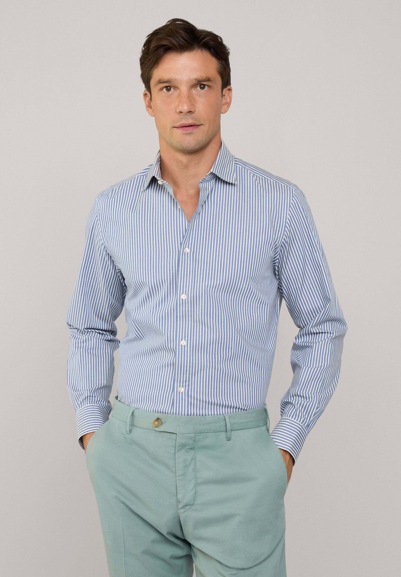Camicetta a righe blu e bianche con maniche lunghe e colletto, abbinata a pantaloni verdi chiari. Tessuto liscio e design aderente.