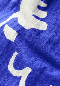 Tessuto blu con una trama a costine che presenta ampie forme astratte bianche. Il design include una pronunciata "Y" stilizzata e ulteriori forme geometriche.