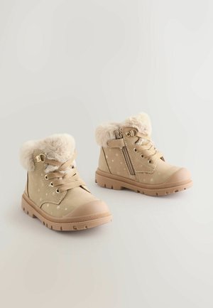 Beiga ankelboots med ett syntetiskt pälskrage, snördesign, sidodragkedja och stjärnmönster. Gummisulor för grepp och hållbarhet.