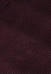 Tissu bordeaux texturé présentant des motifs ondulés et horizontaux en relief, créant une surface douce et tactile. Léger et flexible.