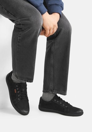 Czarne sneakersy z zamszu i skóry. Zaokrąglony nosek, sznurowany fason, kontrastowe panele o fakturze, noszone z ciemnymi dżinsami i szarymi skarpetkami.