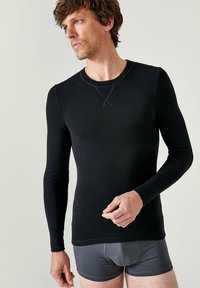 Zwarte langarmshirt gemaakt van gladde stof, met een ronde halslijn met contrasterende stiksels en aansluitende mouwen. Draagt met grijze boxershort.
