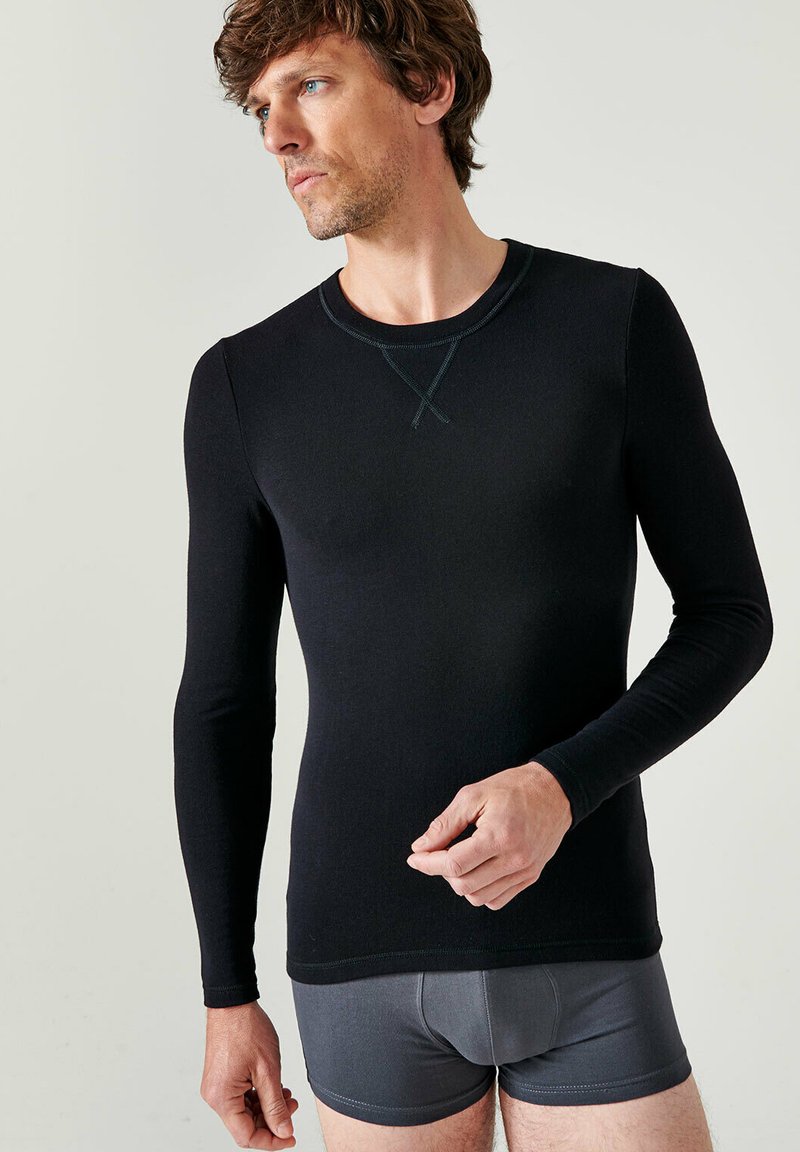 Zwarte langarmshirt gemaakt van gladde stof, met een ronde halslijn met contrasterende stiksels en aansluitende mouwen. Draagt met grijze boxershort.