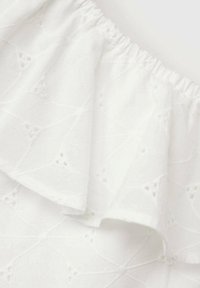Tessuto bianco ricamato con un bordo arricciato. La texture include delicati motivi a occhiello e disegni geometrici su tutta la superficie.