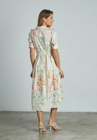 Abito midi stampato floreale in crema, con maniche a palloncino, vita cintrata e dettagli botanici in rosa, verde e arancione.