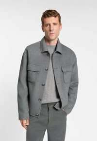 Grå uldblandet jakke med to forlommer, knaplukning og krave. Bruges over en tekstureret grå striktrøje.