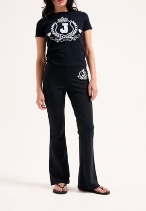 T-shirt nero a maniche corte con grafica bianca e pantaloni corti, abbinati a pantaloni a palazzo neri con dettaglio del logo coordinato e infradito.