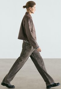 Brun lædercropped jakke over en stribet top, kombineret med løse brune denimjeans og sorte sko, hvilket giver et afslappet look.