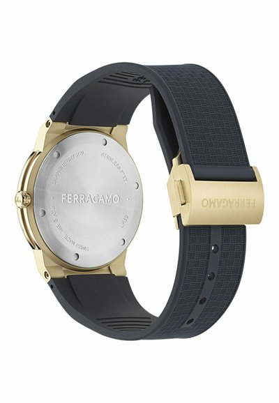 Zelta un sudraba Ferragamo pulksteņa aizmugure ar melnu teksturētu gumijas siksniņu un zelta aizdari, iegravēts ar zīmola nosaukumu.