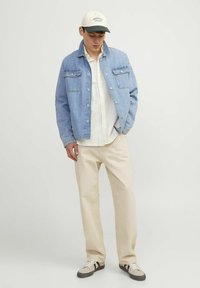 Chaqueta de mezclilla azul claro con cierre de botones en el frente, dos bolsillos en el pecho, camisa blanca a rayas, pantalones crema y zapatillas grises con detalles negros.