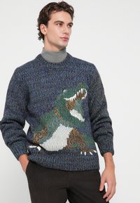 Pulover tricotat în nuanțe de albastru și verde, cu un design de dinozaur pe față. Guler și mâneci cu bordură, cu un finisaj texturat.