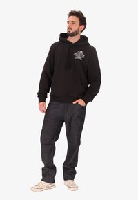 Felpa nera con cappuccio e stringa, tasca frontale e dettagli in bianco, abbinata a jeans denim scuri e sneaker bianche.