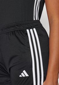 Black athletic pants featuring three white stripes down the sides and an Adidas logo. Material appears smooth and lightweight.